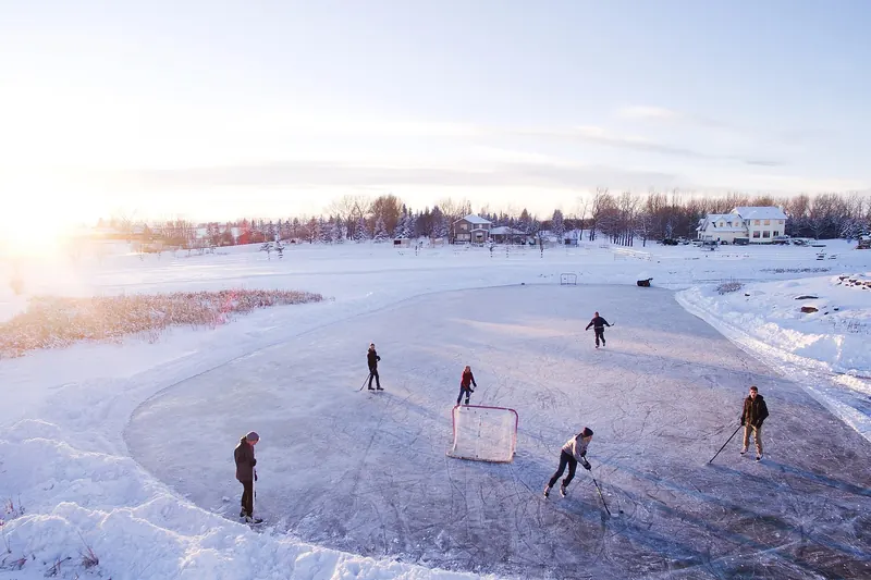 Eisfläche im Freien bei tiefstehender Sonne, im Hintergrund ein Tor und einzelne Spielende