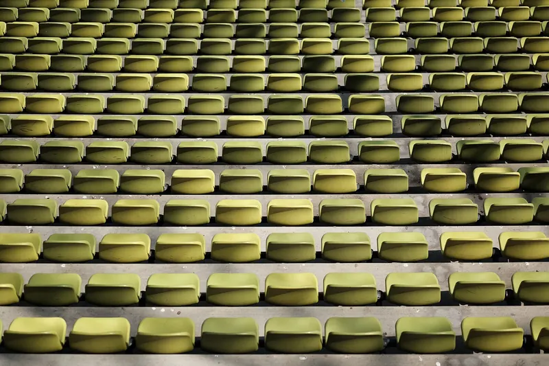 Diagonal ansteigende Reihen gelber Sitzschalen in einem leeren Stadionrang